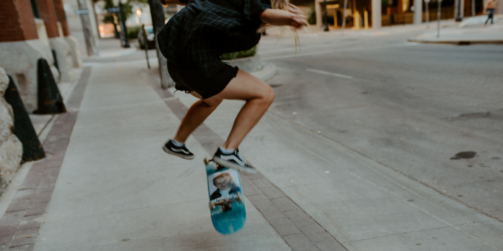 Photo of girl skateboarding on downtown sidewalk, doing a kickflip.